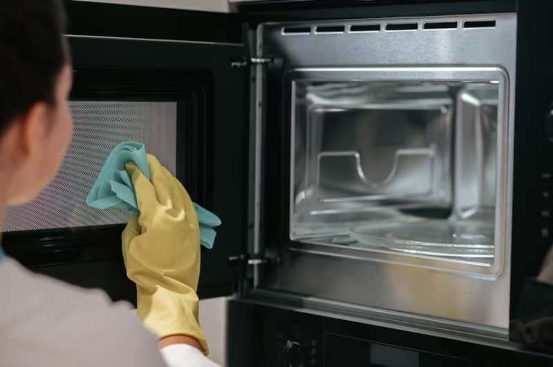 Woman with yellow gloves cleaning the inside glass door of an oven