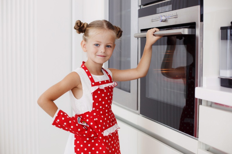 A little girl is grabbing oven glass door