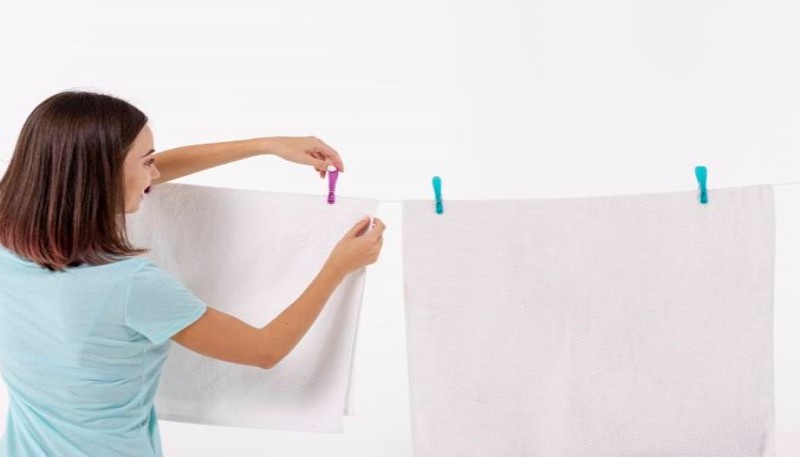 A woman wearing a white shirt is drying towels by putting them on a string